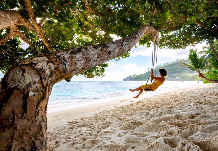Image shows a young woman enjoying a beach swing at Kempinski Seychelles Resort